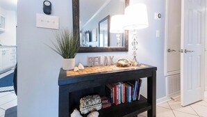 A hallway with a console table, books, decorative items, a mirror, and a door.