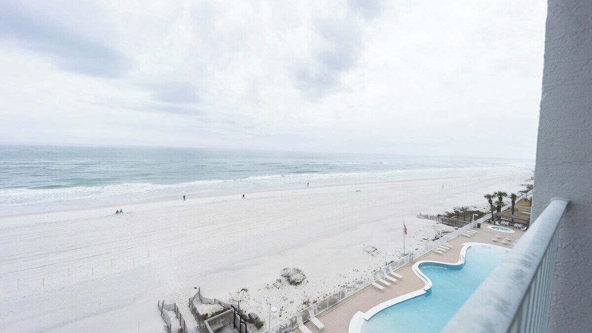 Blick auf den Strand vom Balkon, mit Pool und Liegestühlen.