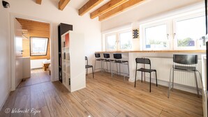 Eine moderne Küche mit Holzbalken, einem Essbereich mit vier Stühlen und Blick durch große Fenster ins Freie.