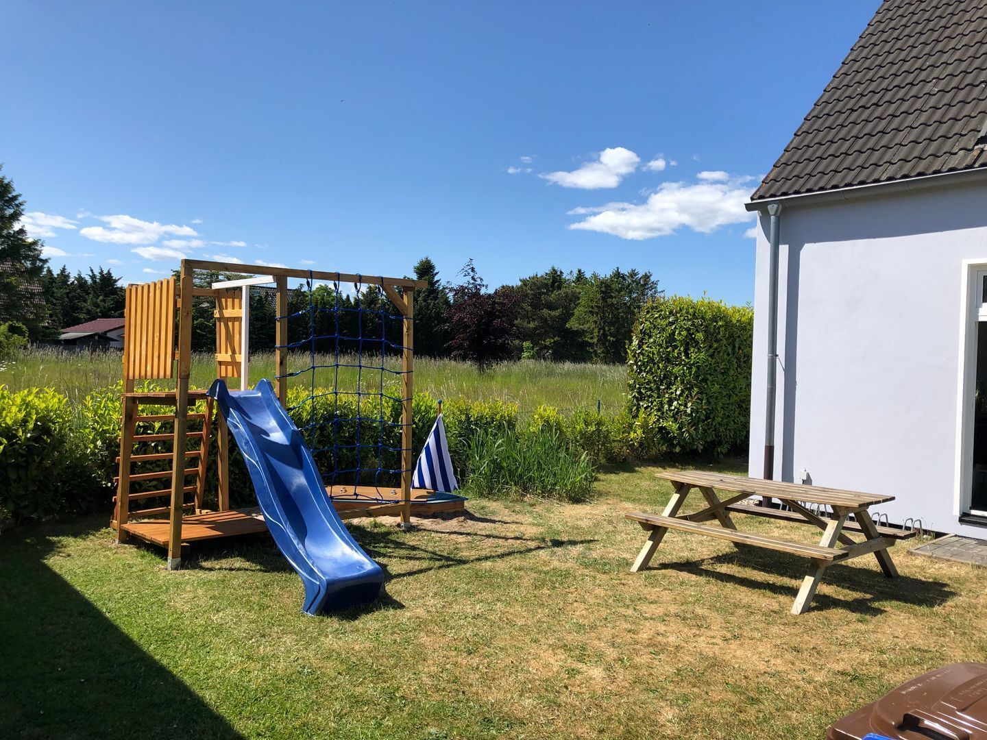 A backyard with a wooden play structure, including a slide, a small flag, and a picnic table.