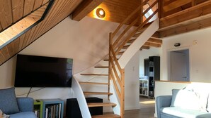 Ein modernes Wohnzimmer mit einer Holztreppe, einem Flachbildfernseher und zwei Sofas.