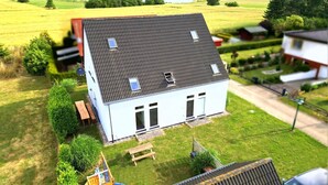 Ein zweistöckiges Haus mit geneigtem Dach, ein kleiner Garten mit einer hölzernen Bank und einer Spielanlage.