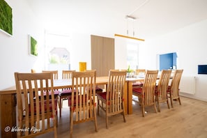 A dining area with a wooden table and chairs, a vertical wooden slat partition, and a hanging light fixture. - Ferienhaus Look - Ferienhaus Look auf der Insel Rügen (Garz/Rügen)