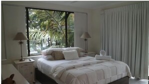 Una camera da letto con un'ampia finestra, un letto con biancheria bianca, due comodini e un tavolino da notte.