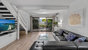 Un salon moderne avec un canapé en cuir, une table basse en verre et un téléviseur à écran plat posé sur un meuble blanc.
