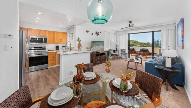 Una cocina moderna con electrodomésticos de acero inoxidable, un comedor con mesa de vidrio y una sala de estar con sofá azul y un ventanal grande.