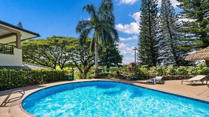 Una piscina azul cristalina con cubierta de madera, rodeada de abundante follaje y árboles altos.