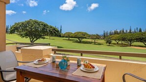 Un balcón con una mesa de madera dispuesta para el desayuno, con vista a un campo de golf con árboles y cielo despejado.