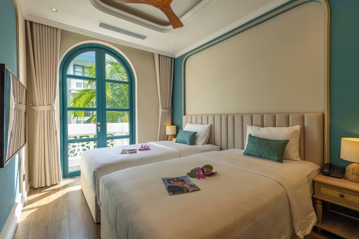 Habitación de hotel con dos camas, un ventanal grande y vistas a zonas verdes.
