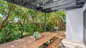 Eine Holzterrasse mit Tisch und Stühlen, umgeben von üppiger Vegetation und einem Holzzaun.