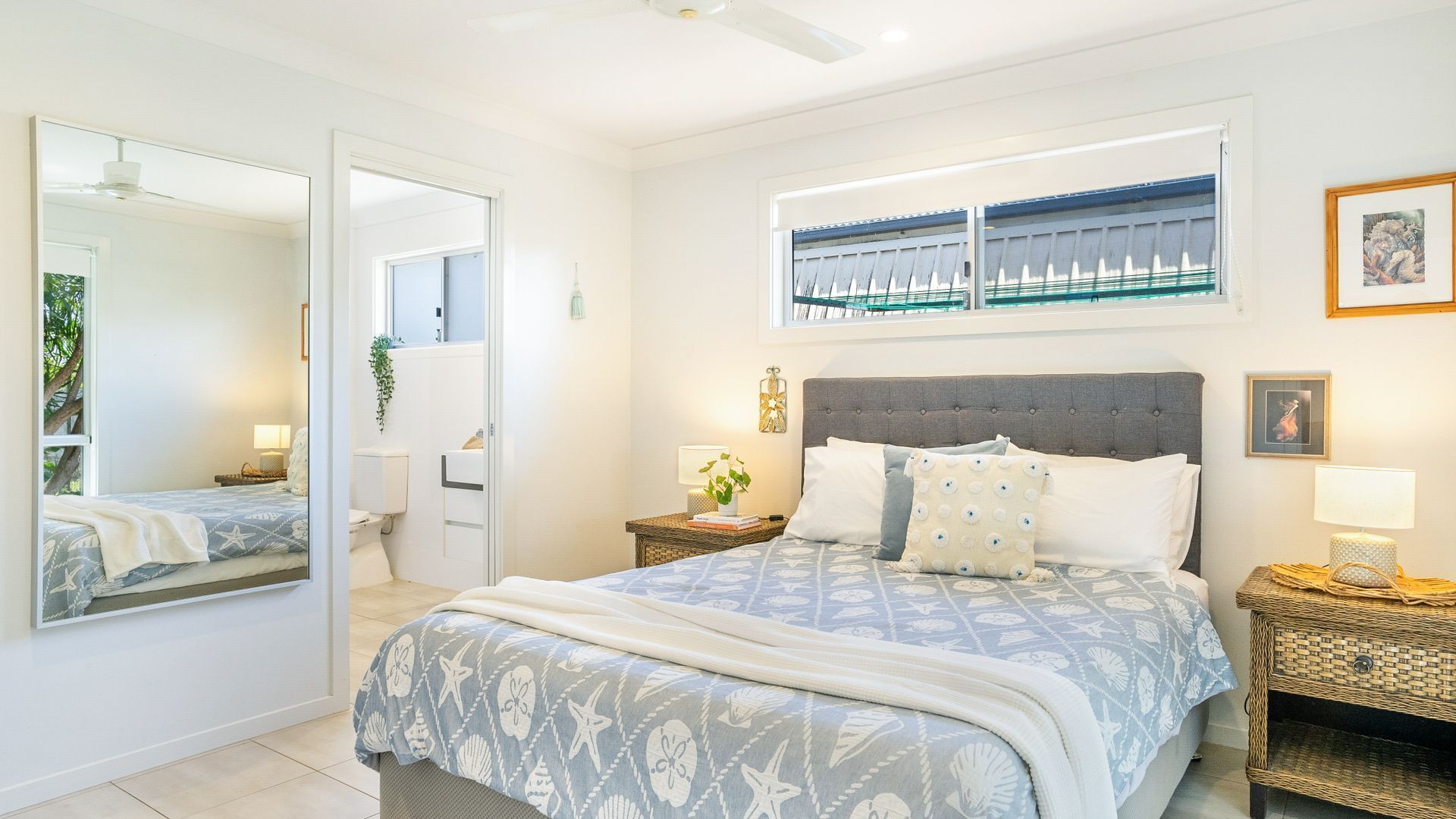 Une chambre à coucher avec un grand lit, une table de chevet, un miroir et une fenêtre donnant sur une balustrade bleue.