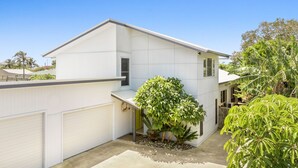 Ein modernes, zweistöckiges Haus mit Garage, umgeben von üppigem Grün und Palmen.