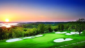 En golfbana med utsikt över solnedgången, omgiven av träd och en vattenyta.