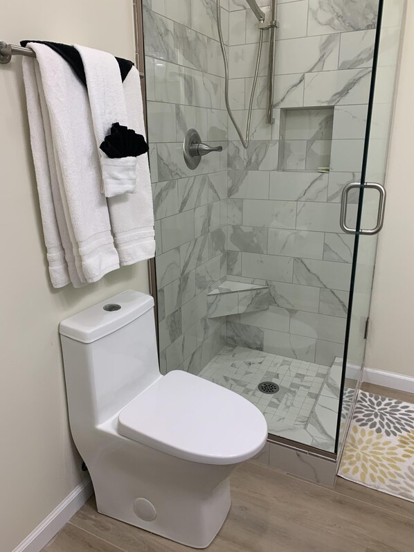 A modern bathroom with a glass-enclosed shower, a white toilet, and a towel rack with multiple towels. - Spectacular Lake Views/Close to Big Cedar (Ridgedale)