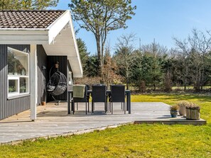Ein modernes Haus mit einer Holzterrasse, Sitzgelegenheiten im Freien und einem Hängesessel.