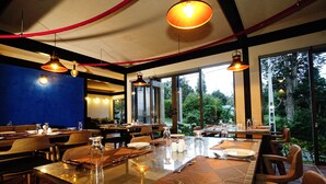 A restaurant with a large glass table, wooden chairs, and hanging pendant lights. - Hotel Bulwark (Nuwara Eliya)