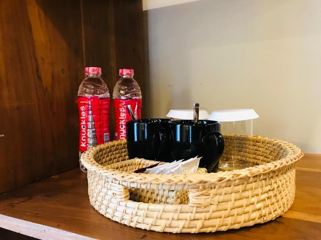 Una cesta tejida sobre una estantería de madera con dos botellas de refresco Knuckles y dos tazas negras.