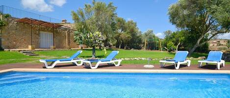 A swimming pool with blue water, surrounded by lounge chairs and a stone building with a metal roof.
