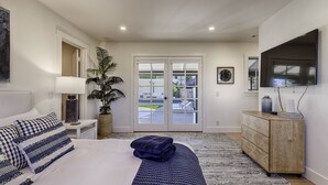 A bedroom with a bed, bedside table, lamp, potted plant, dresser, and a TV. - Modern Ranch House-swim, soak, pickleball & walk to wineries (Sonoma)