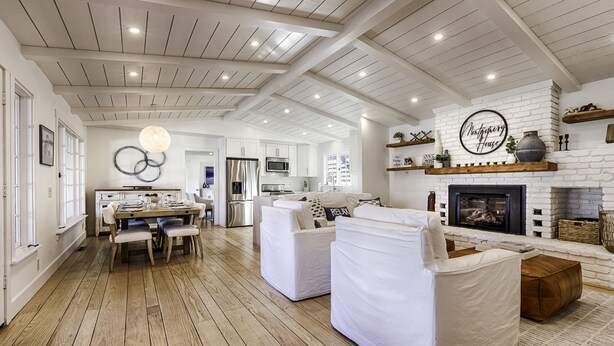 A spacious living room with white furniture, a fireplace, and a kitchen in the background. - Modern Ranch House-swim, soak, pickleball & walk to wineries (Sonoma)