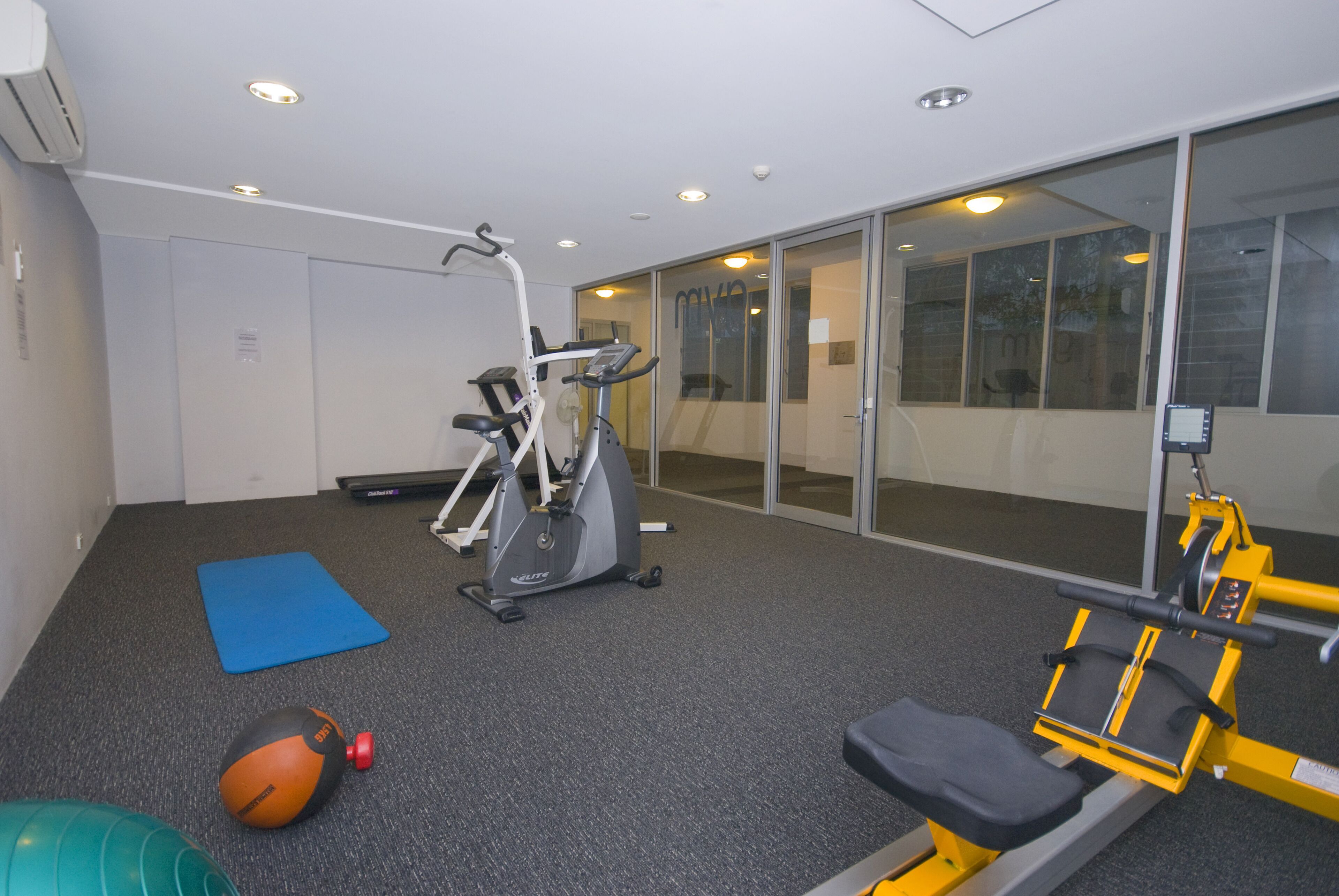 Un gimnasio con equipo de ejercicio, una colchoneta azul y una pelota medicinal.