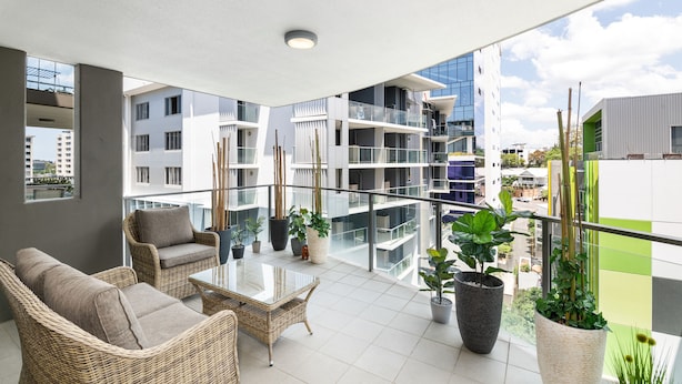 A balcony with wicker furniture, potted plants, and a view of surrounding buildings. - Allegro Apartments (South Brisbane)