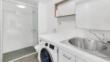 A modern bathroom with a glass-enclosed shower, a built-in washing machine, and a stainless steel sink.