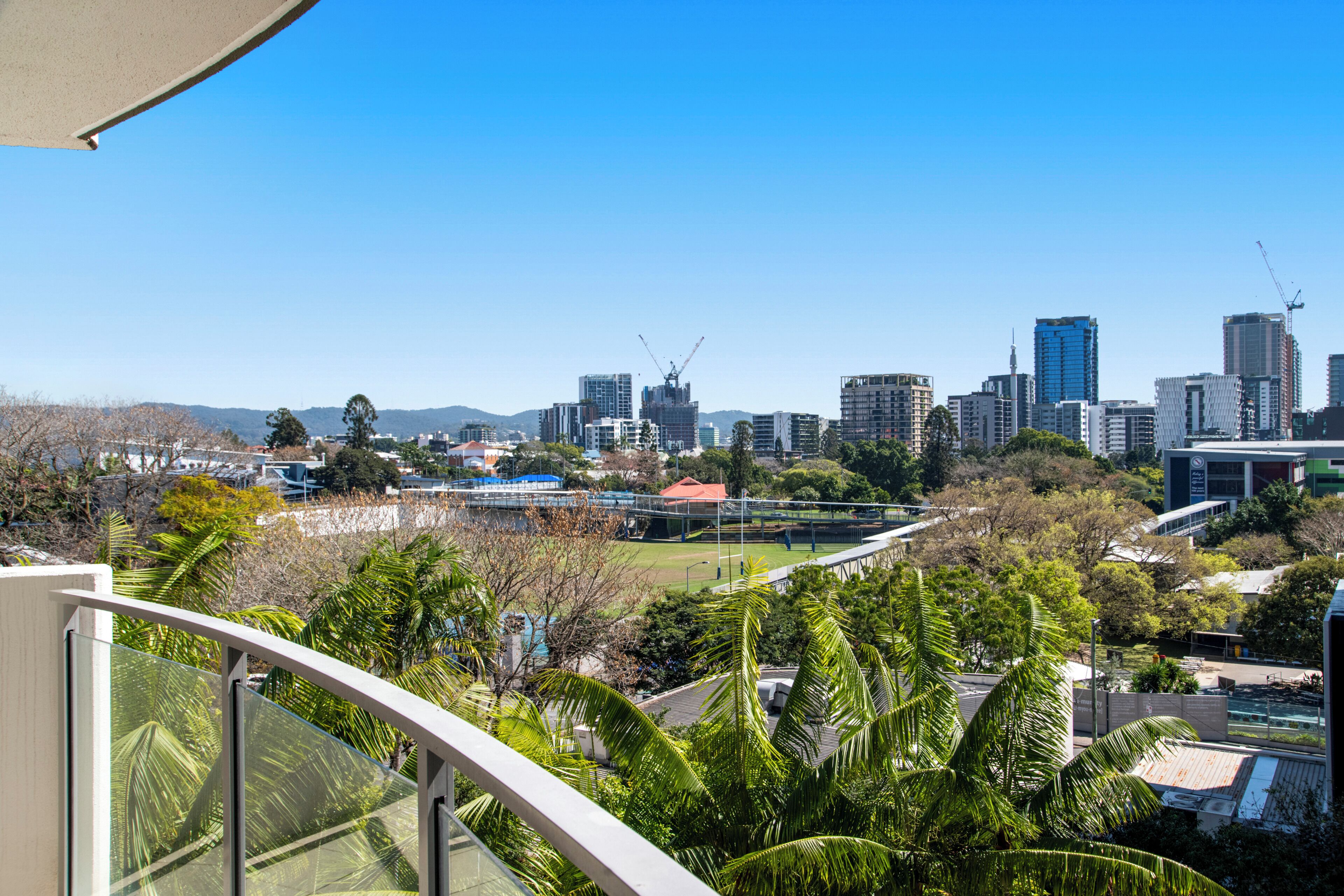 A city skyline with modern buildings, a construction crane, and a park with palm trees.