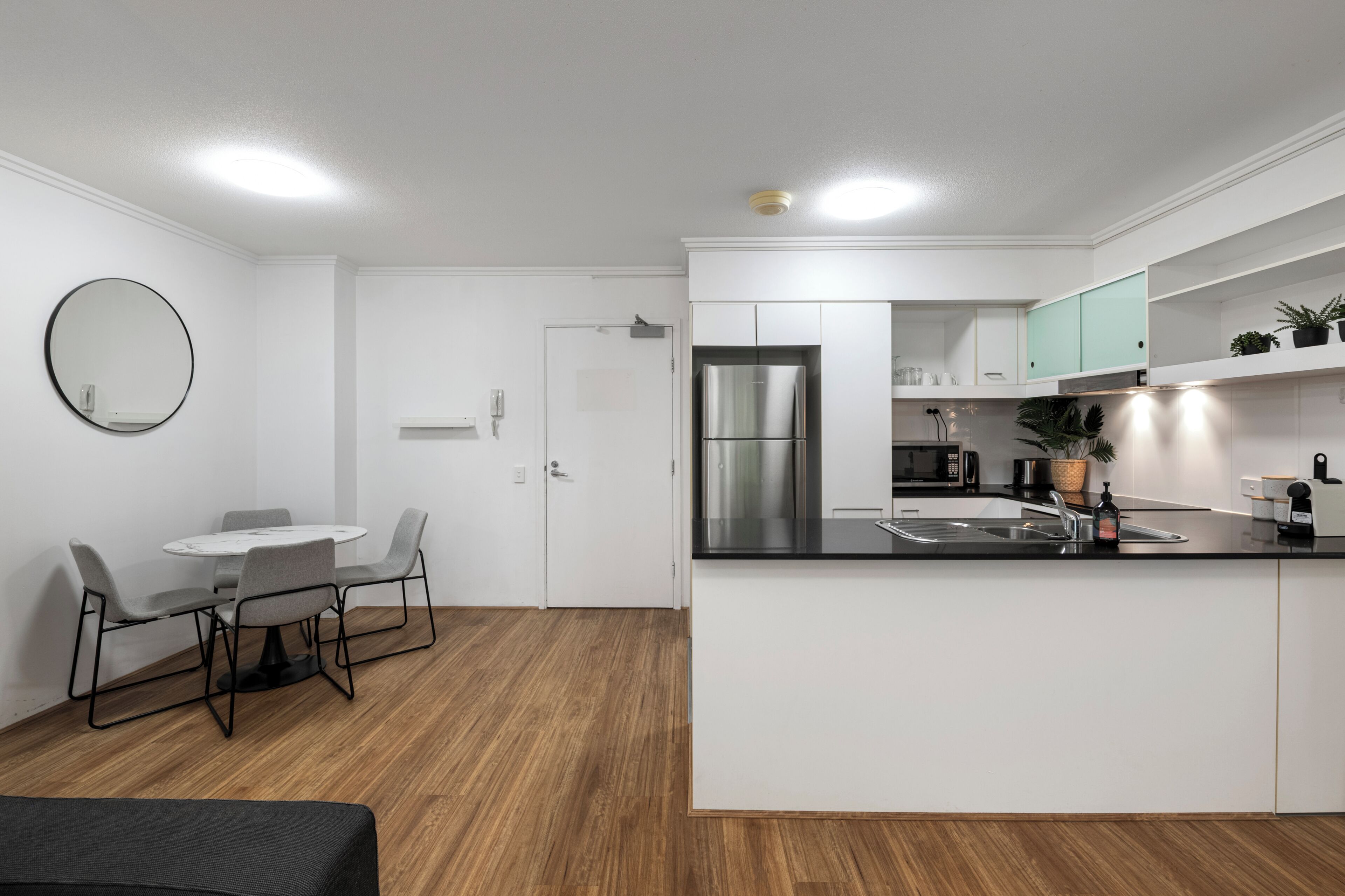 A modern kitchen with white cabinets, a stainless steel refrigerator, and a dining area with a round table and chairs.