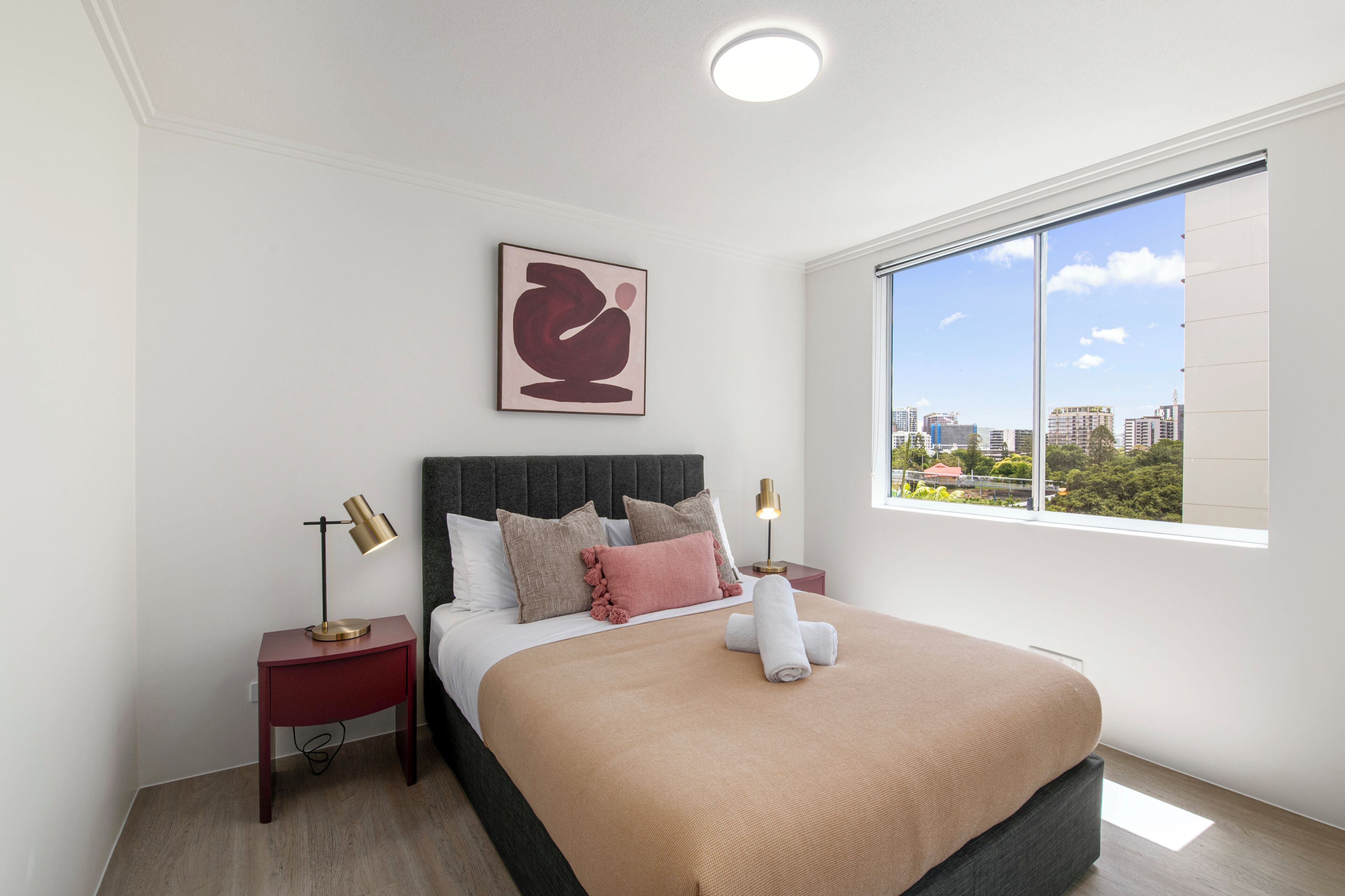 A modern hotel room with a large bed, two bedside tables, a city view, and a ceiling light.