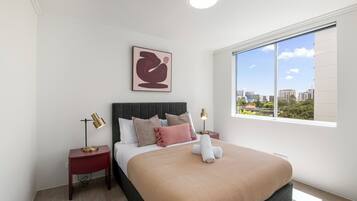 A modern hotel room with a large bed, two bedside tables, a city view, and a ceiling light.
