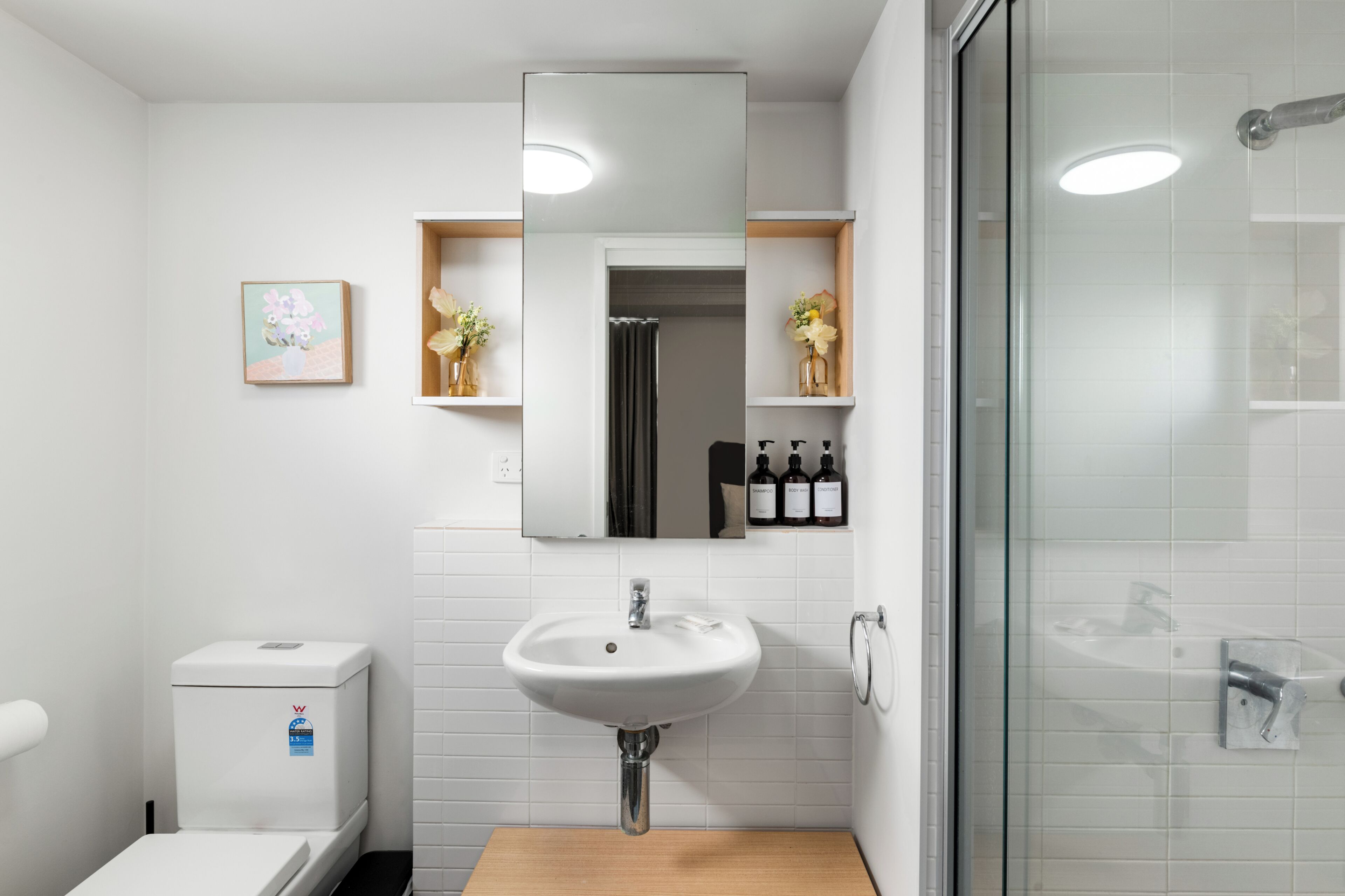 A modern bathroom with a white sink, a toilet, a shower, and a mirror.