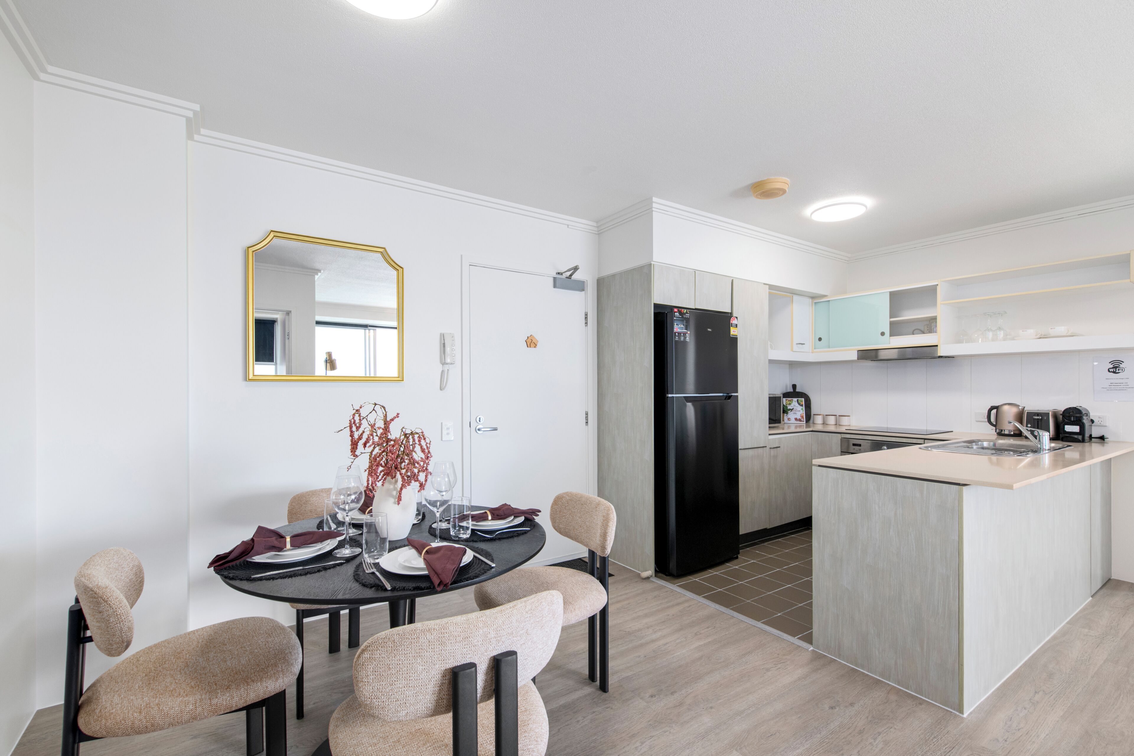 Cozinha moderna com ilha central, área de jantar com mesa redonda e cadeiras, e um espelho grande na parede.