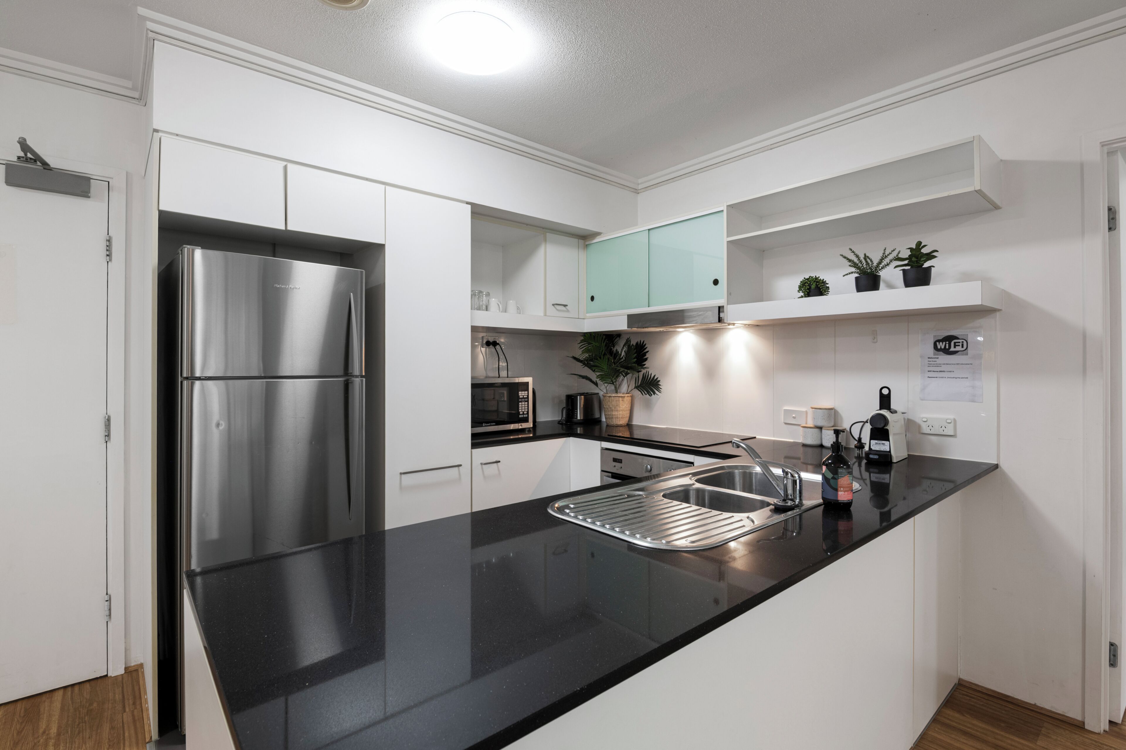 A modern kitchen with white cabinets, a stainless steel refrigerator, a black countertop, a sink, and a microwave.