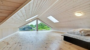 A spacious attic bedroom with wooden floors and sloped ceilings, featuring skylights and a view of a house and greenery outside.