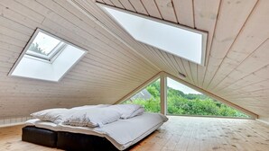 A bedroom with a sloped ceiling, skylights, a bed, and a view of greenery outside.