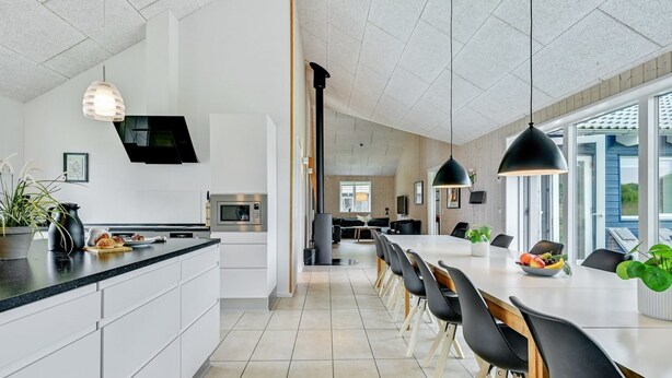 A modern kitchen with a central island, a dining area with a long table and chairs, and a view of the outdoors through large windows.