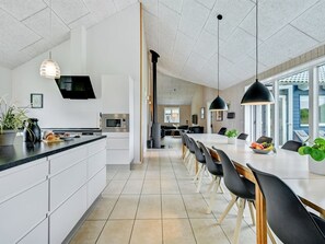 A modern kitchen with a central island, a dining area with a long table and chairs, and a view of the outdoors through large windows. - "Jelke" - 520m from the sea by Interhome (Tranekær)