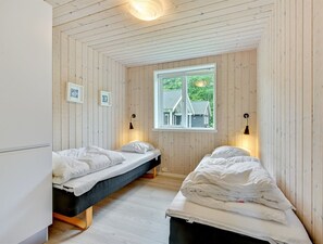 A room with two beds, wooden walls, a window with a view, and wall-mounted lamps.