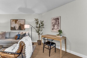Ein Wohnzimmer mit einer Couch, einem Couchtisch, einer Lampe, einem Schreibtisch und einem Sessel.