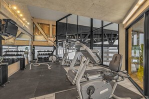 Ein Fitnessraum mit Trainingsgeräten, einem Fernseher und großen Fenstern.