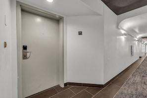 Un pasillo de hotel con una puerta cerrada, un letrero de número y suelo alfombrado.