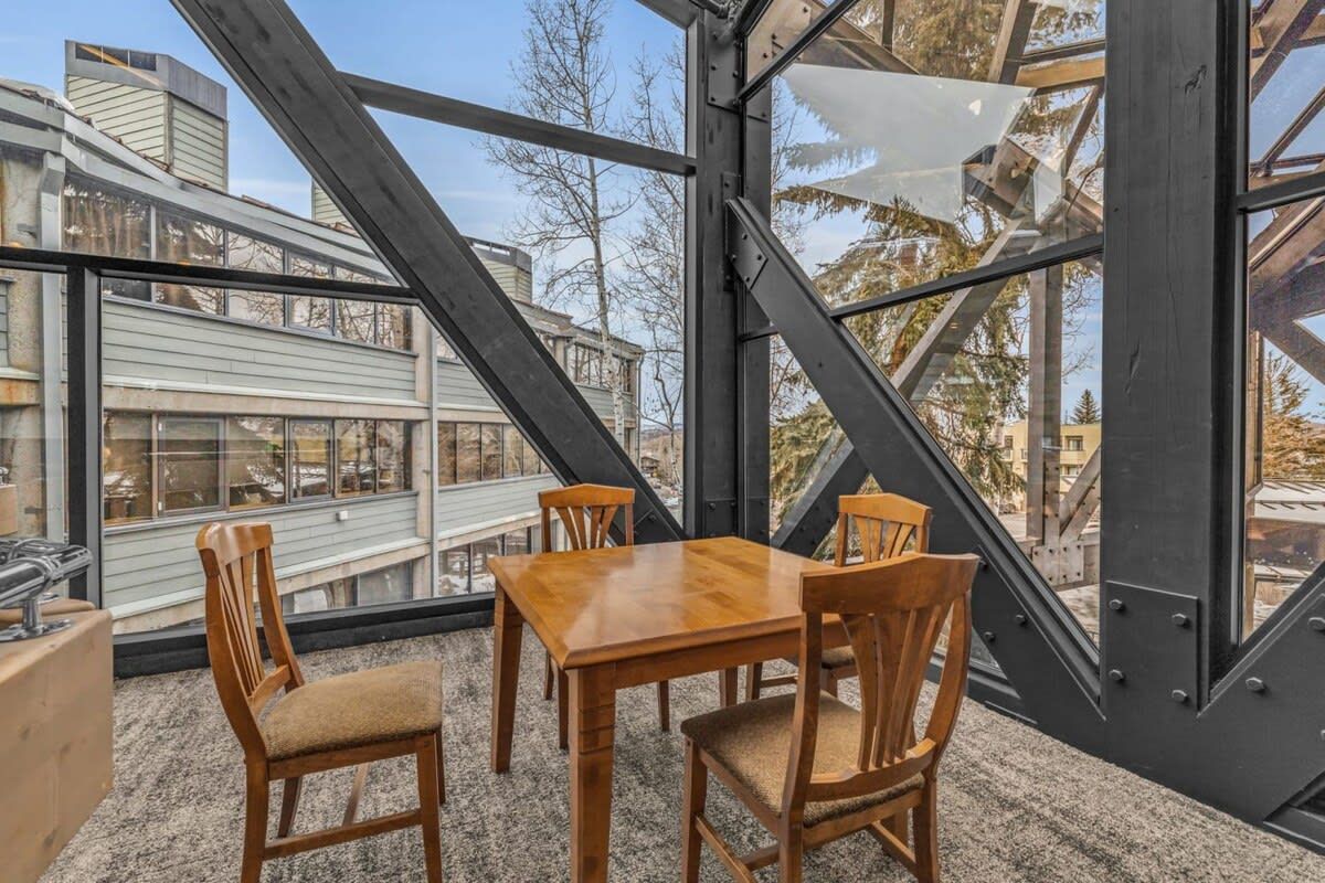 Un comedor con mesa y sillas de madera, ventanas amplias y vistas a edificios.