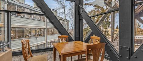 Un comedor con mesa y sillas de madera, ventanas amplias y vistas a edificios.