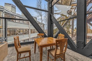 Ein Essbereich mit Holztisch und -stühlen, großen Fenstern und Blick auf Gebäude.