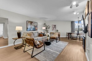 Una sala de estar moderna con un sofá, dos sillones, una mesa de centro y un comedor con una mesa y sillas.