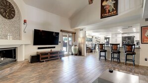 A spacious living room with a fireplace, a large flat-screen TV, and a dining area with bar stools. - Scottsdale Kierland Compound (Scottsdale)