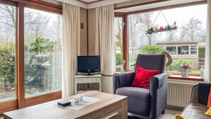 A cozy room with a large window, a desk with a computer, a comfortable chair, and a view of a garden and a house outside. - Nice (sta)caravan in Reutum with WiFi (Reutum)