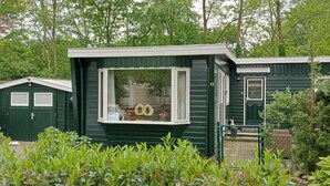 A green mobile home with a large window, a small porch, and a fenced garden area. - Nice (sta)caravan in Reutum with WiFi (Reutum)