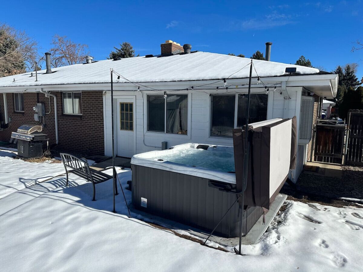Una casa con jacuzzi en el jardín trasero, rodeada de nieve.